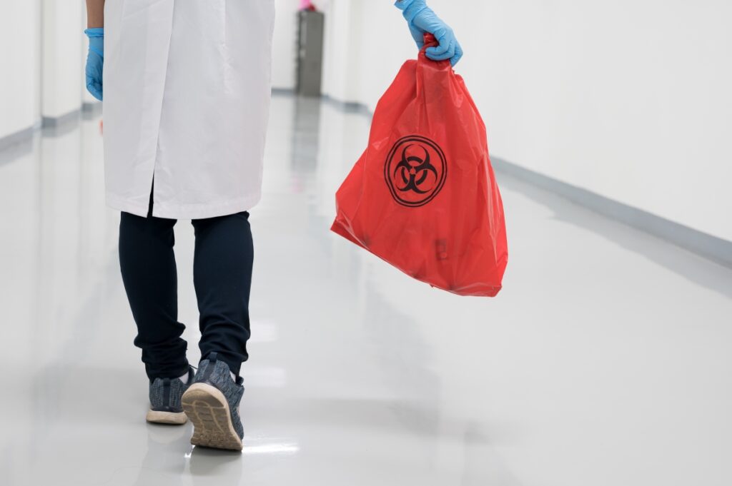 A person in a white coat holding a red bag of medical waste