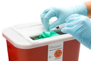 Gloved hand throwing away sharps in a medical waste container for disposal